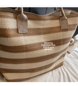 Detail of reinforced cross-stitched handles on a striped woven straw tote bag