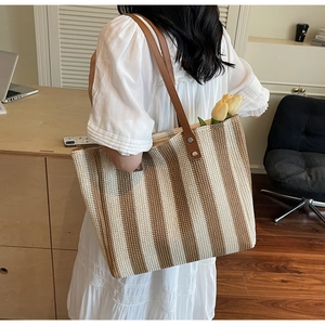 Detail of handwoven straw tote bag with brown leather straps and vertical stripes