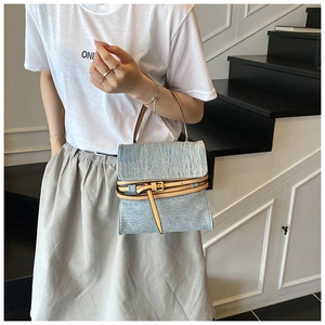 Detail of light blue denim tote bag with camel faux leather trim and retro buckle strap