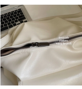 Close-up of smooth charcoal grey metal zipper on textured cream leather tote bag