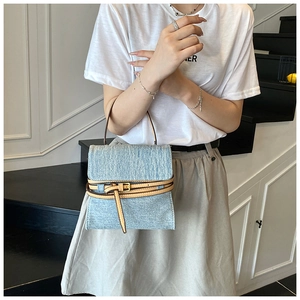 Detail of light blue denim handbag with brown leather trim and metal belt buckle design
