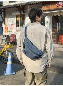 Rear view of a blue washed denim crossbody bag on model in an urban outdoor setting