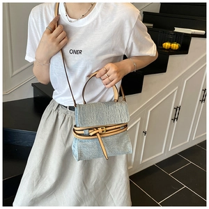 Detail of blue denim crossbody bag with leather straps and metal buckle on casual model