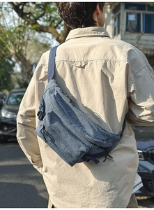 Detail of blue washed denim crossbody bag with multiple zip pockets and adjustable strap