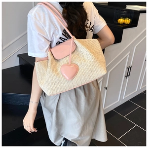 Detail of hand-woven straw tote with pink leather straps and heart charm on a model