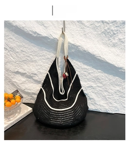 Close-up of a black and white woven tote bag with a strawberry charm on a stone wall