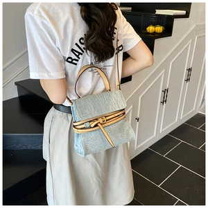 Detail of light blue denim handbag with brown leather accents shown on a model