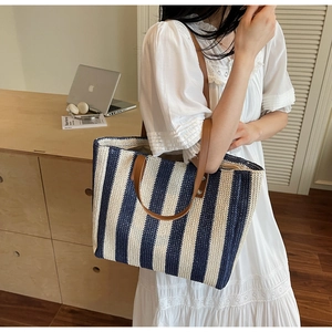 Detail of navy blue striped straw tote bag featuring brown leather handles and rivets
