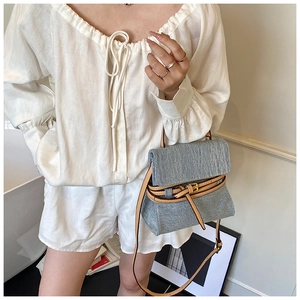 Detail of light blue denim texture and brown leather strap on a small square crossbody bag