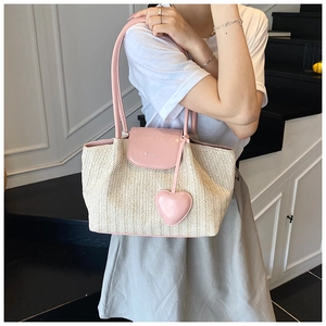 Detail of woven straw tote bag featuring pink leather straps and a heart pendant charm