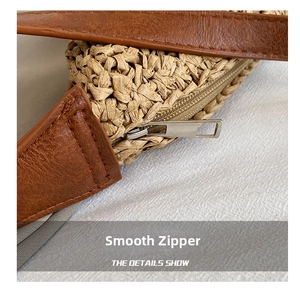 Detail view of smooth metal zipper and leather trim on woven straw shoulder bag