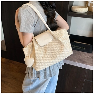 Detail of woven straw tote bag featuring white leather flap and cute heart charm accessory