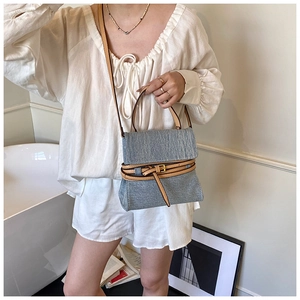 Detail of blue denim tote bag featuring brown leather straps and metallic buckle