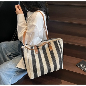 Detail view of black and white striped woven tote bag with brown leather handles and rivets