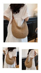 Detail of a large woven straw hobo bag featuring a brown leather adjustable shoulder strap
