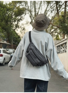 Outdoor shot of a man wearing a dark grey washed denim crossbody bag with dual zippers