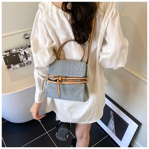 Detail of light blue denim handbag with brown leather straps shown on a model