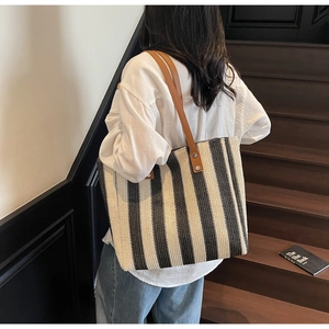 Detail of the woven vertical striped tote bag with brown leather straps and metal rivets
