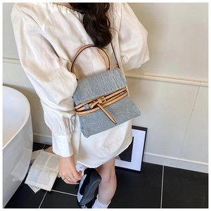 Detail shot of blue denim handbag with brown leather trim and adjustable shoulder strap