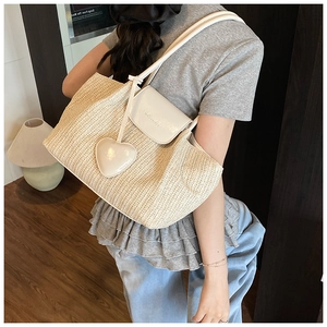 Detail of hand-woven straw tote with white leather flap and cute heart charm accessory
