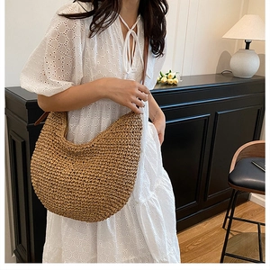 Detail view of woven hobo straw bag with dark leather strap on white lace dress