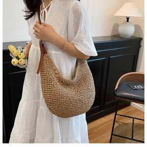 Side view of large straw crescent shoulder bag with brown leather strap on model