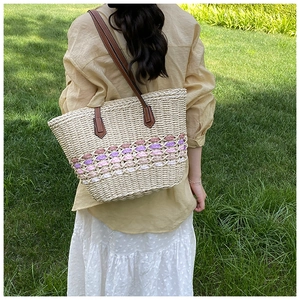 Detail of handwoven straw tote featuring pink and purple hollow-out pattern and leather strap