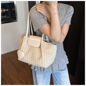 Detail of straw woven tote with cream leather flap and heart pendant charm