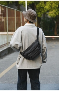Detail of dark grey washed denim chest bag with adjustable strap worn on urban street