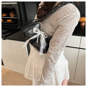 Détail du sac demi-lune noir avec grand nœud en dentelle blanche et chaîne de perles fines