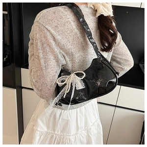 Detailed view of black pleated cloud bag with pearl bow and lace trim on a shoulder strap