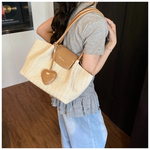 Detail of hand-woven straw tote bag featuring a leather heart pendant and branded flap