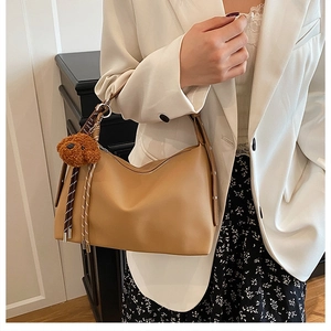 Détail du sac sous l'aisselle camel en cuir mat avec un pendentif d'ours en peluche mignon