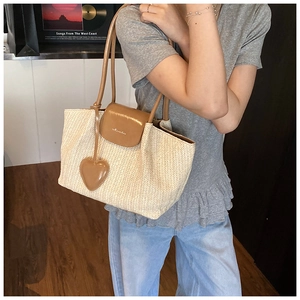 Detail of hand-woven straw tote with brown leather flap and heart-shaped charm accessory