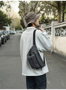 Detail of dark grey washed denim sling bag with zippers worn in a street style setting