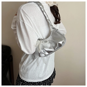 Détail du sac métallisé argenté avec nœud en dentelle, perles et bandoulière plissée