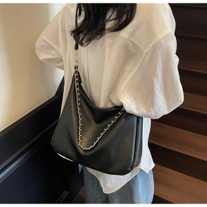 Close-up of black lychee leather hobo bag with gold chain strap on a model's shoulder