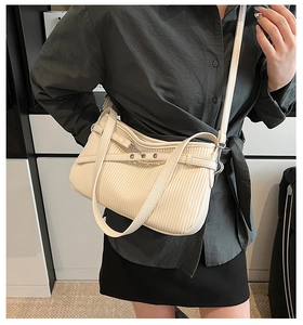 Détail du sac crème plissé avec plis verticaux et décoration d'œillets métalliques