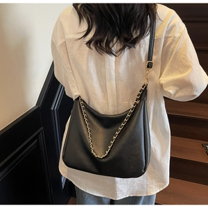 Close-up of black lychee texture dumpling bag with gold chain strap worn by a model