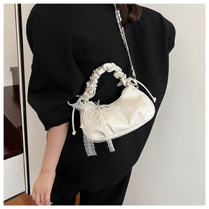 Detail of cream pleated cloud bag featuring pearl lace bow charm and chain strap