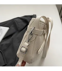 Detailed view of silver metal hardware and lychee grain leather on off-white shoulder bag