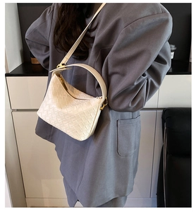 Close-up of white woven leather handbag with gold hardware worn by a model in a gray suit