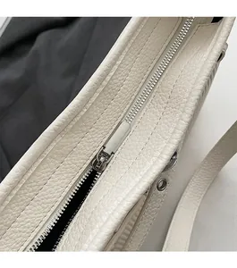 Detailed macro of smooth silver metal zipper and lychee grain texture on white leather bag