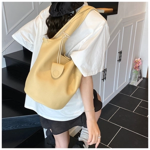 Detailed view of yellow lychee pattern leather bucket bag with wide strap on a model