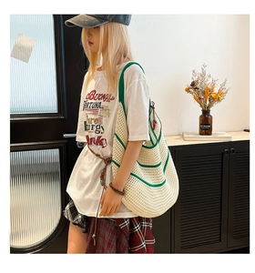 Close-up of the large hollow knit tote bag with green stripes on a shoulder model
