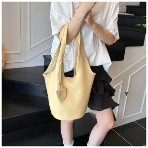 Close-up of light yellow bucket bag featuring pebble leather texture and a matching charm
