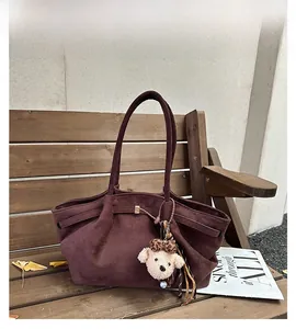 Detailed view of brown suede tote bag featuring a cute plush dog charm on a wooden bench