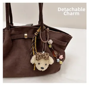 Detail of a brown suede tote bag with a detachable plush dog charm and beaded chain