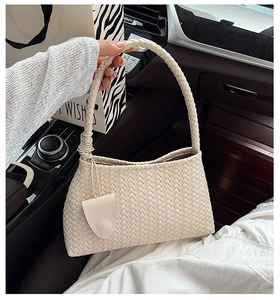 Close-up of cream woven shoulder bag with knotted handle detail in a car interior