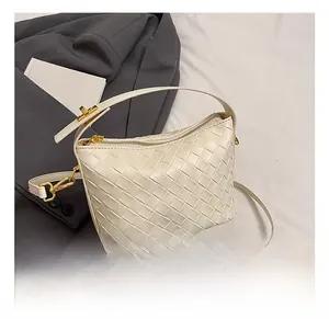 Detailed view of woven leather texture on cream handbag with gold zipper and strap